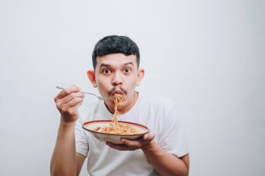 Genç bir adam arkaplanda neşeli bir ifadeyle lezzetli hazır eriştelerin tadını çıkarıyor..