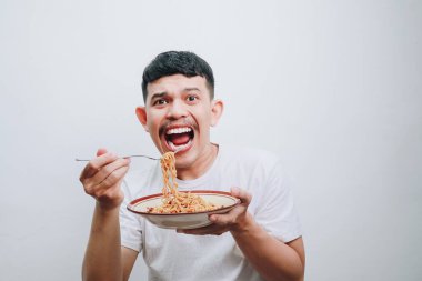 Neşeli, genç bir adam kaseden şehriye yiyor, heyecan ve mutluluk sergiliyor..