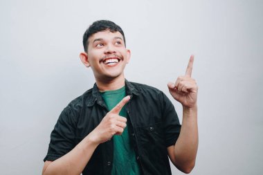 Neşeli genç bir adam tavanı işaret ederken heyecanını ifade eder..