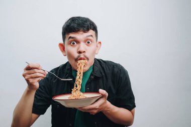 Genç bir adam kaseden erişte yemekten zevk alır, neşe ve heyecan gösterir..