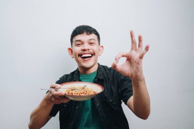 Genç bir adam güzel bir jest yaparken bir kase erişteden zevk alır..