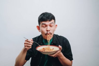 Genç bir adam bir kase erişteye dalmış, neşe ve heyecan sergiliyor..