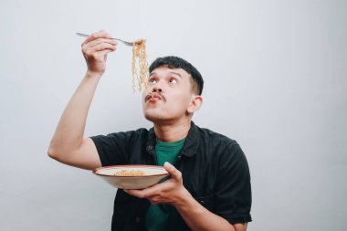 Bir adam her ısırıkta neşeyle bir kase erişteden zevk alır..