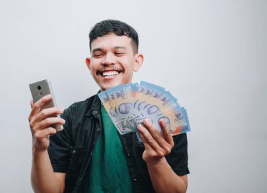 Genç bir adam sevinçle elinde nakit para ve akıllı bir telefon tutar. Heyecan ve pozitiflik sergiler..
