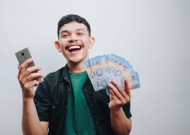 Parası ve akıllı telefonu olan neşeli bir genç adam finansal başarısını kutluyor..