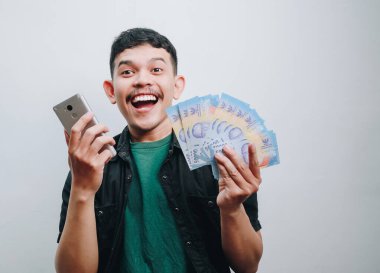 Neşeli genç bir adam elinde para ve akıllı bir telefonla mutluluk saçıyor..