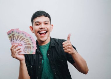 Neşeli genç bir adam başparmak işareti ile nakit sergiliyor..
