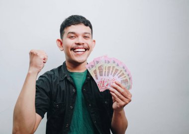 Neşeli genç bir adam elinde parayla kutlama yapıyor, mutluluğu gösteriyor..