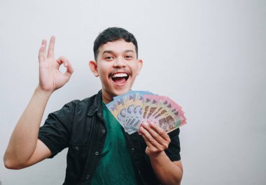 Genç bir adam para tutarak mutluluğunu ifade eder, finansal zaferi simgeler..