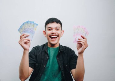 Neşeli genç bir adam gururla para sergiliyor, mutluluk ve heyecan saçıyor..