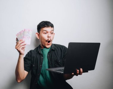 Genç bir adam dizüstü bilgisayarı üzerinde çalışırken finansal bir sürprizi kutluyor..