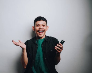 Neşeli genç bir adam akıllı telefonuyla öylesine meşgul olurken geniş bir gülümseme sergiliyor..