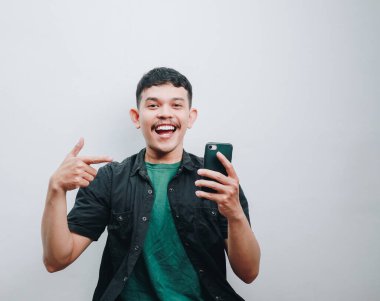 Neşeli genç bir adam telefonla poz veriyor, neşe ve heyecan saçıyor..