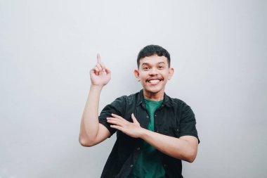 Neşeli bir genç adam minimalist bir stüdyo ortamında neşeli bir gülümsemeyle yukarıya doğru işaret eder..