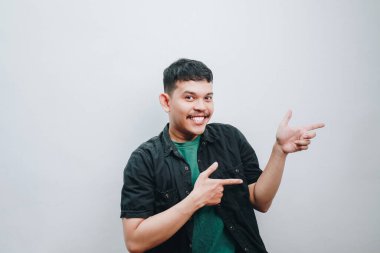 Neşeli bir genç adam gülümsüyor ve neşeli bir şekilde işaret ediyor..