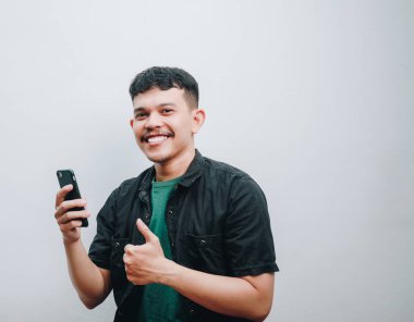 Genç bir adam gülümsüyor ve akıllı telefonu tutarken başparmağını kaldırıyor..