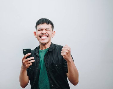 Neşeli bir genç adam, akıllı telefonuyla kutlama yaparken neşesini ifade eder..