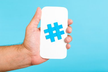 Bir hashtag sembolünü gösterirken el / beyaz kağıt ile mavi arka plan ile telefon telefon şekil üzerinde oturum. Internet, sosyal medya kavramı.