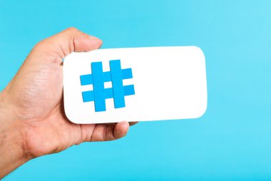 Bir hashtag sembolünü gösterirken el / beyaz kağıt ile mavi arka plan ile telefon telefon şekil üzerinde oturum. Internet, sosyal medya kavramı
