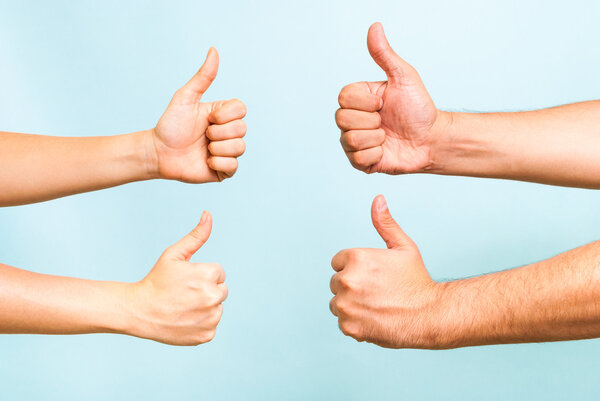 Successful team concept. Four hands making thumbs up gesture on blue background.