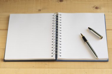 Ahşap masa üzerinde gümüş kalem ile boş defter.