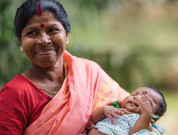 DIAMOND HARBOR, ÍNDIA - 04 de abril de 2013: Mulher indiana rural com criança nas mãos e sorrisos de sari vermelho — Fotografia de Stock