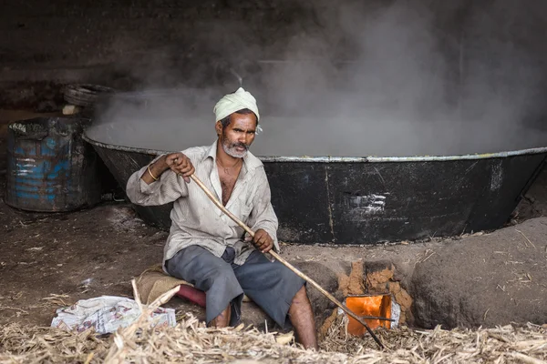 Indian worker boiling sugarcane juice in the big iron pot