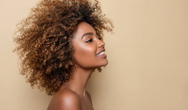 Bej arka planda temiz, sağlıklı bir cildi olan Afro-Amerikan bir kızın güzel portresi. Gülümseyen rüya gibi güzel siyah kadın. Kıvırcık saçlı afro saçlı.