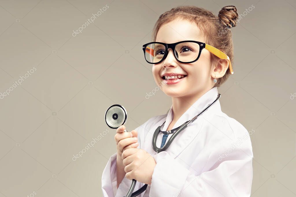 Child girl in a medical gown and stethoscope plays and pretends to be a doctor . Child choose a profession for the future. Happy and smiling baby in the game. Expressive facial emotions