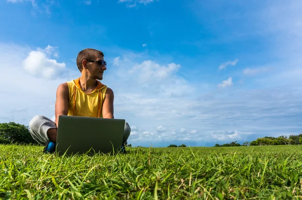Jeune homme assis sur l'herbe et travaillant avec un ordinateur portable — Photo