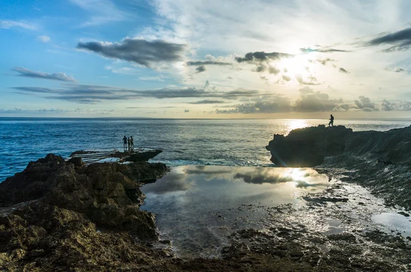 Des gens au bord de la roche près de la mer. Coucher de soleil reflété dans les piscines — Photo
