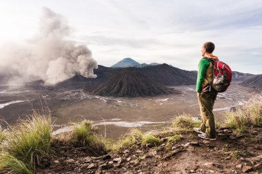 Man on the hill is looking on Bromo volcano eruption. East Java, Indonesia clipart