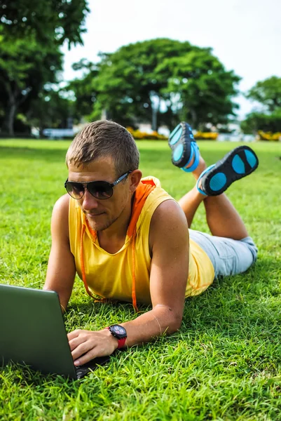 Jeune homme couché sur l'herbe et travaillant avec un ordinateur portable — Photo