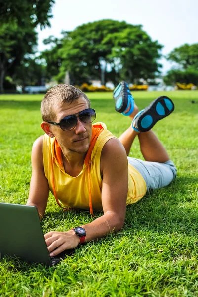 Jeune homme couché sur l'herbe et travaillant avec un ordinateur portable — Photo