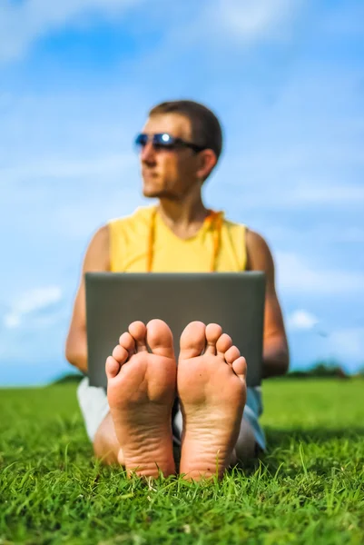 Jeune homme assis sur l'herbe et travaillant avec un ordinateur portable, se concentrer sur les pieds — Photo
