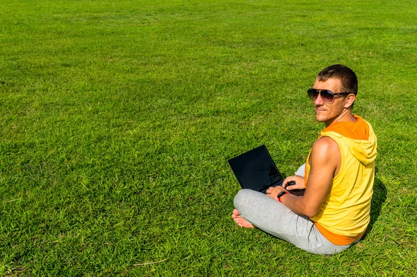 Jeune homme assis sur l'herbe et travaillant avec un ordinateur portable — Photo