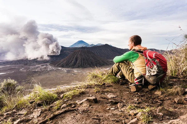 L'homme est assis sur la colline et regarde l'éruption du volcan Bromo. Java Est, Indonésie Photos De Stock Libres De Droits