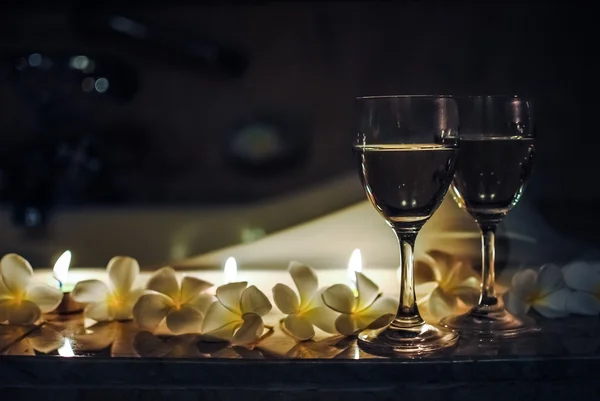 Deux verres à vin avec des fleurs et des bougies au premier plan dans la salle de bain Photo De Stock