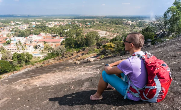 Mladý muž sedí v horách a při pohledu na město — Stock fotografie
