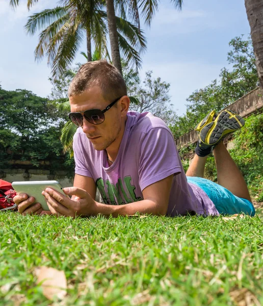 Homme allongé sur l'herbe et utilisant sa tablette — Photo