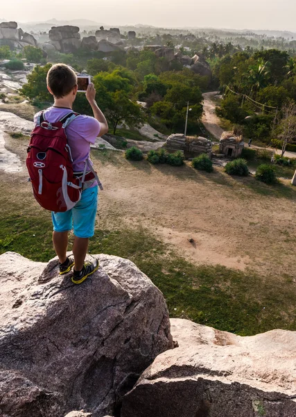 Nuori mies seisoo vuorella ja tekee valokuvan laaksosta — kuvapankkivalokuva