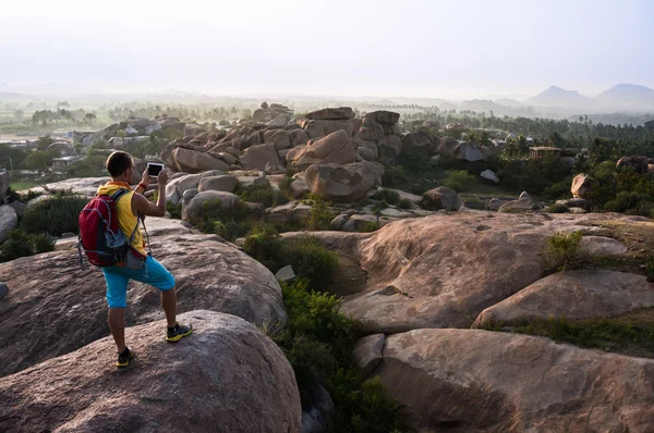 Joven parado en una montaña y haciendo una foto del valle — Foto de Stock