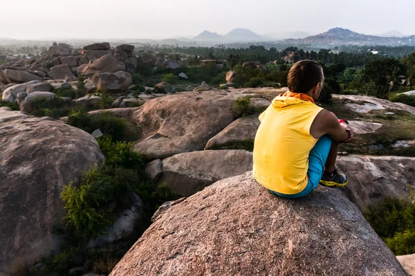 Nuori mies istuu yksin vuoren laidalla ja katsoo eteenpäin. — kuvapankkivalokuva