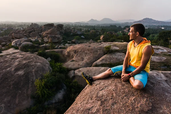 El joven está sentado en la montaña con una hermosa vista y mirando hacia adelante —  Fotos de Stock