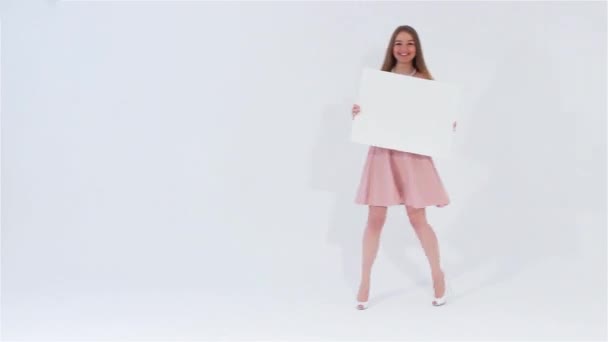 Sonriente chica atractiva en vestido rosa caminando con bandera blanca en blanco — Vídeo de stock