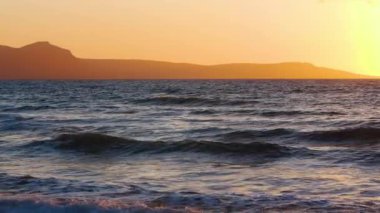 Doğal dramatik deniz manzarası dağların doğuşu, gün batımı altın dalgaların arasından parlayan güneş, okyanus ve deniz ağır çekim 4k