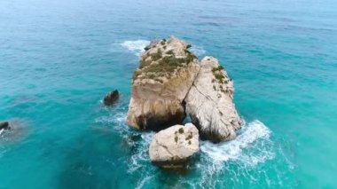 Dalgaların yukarıdan görünüşü mavi bir okyanusta kayalara çarpıyor. Deniz dalgaları güzel kumsalda, hava aracı 4K 'da. Okyanus ıssız dağ kayalarına, turistik yerlere, tatillere ve dinlenmeye çarpıyor.