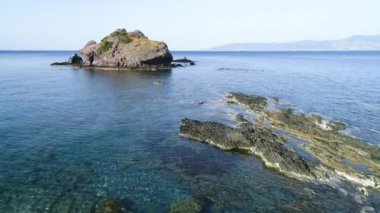 Mavi okyanustaki kayalıkların yukarıdan görünüşü. Deniz dalgaları güzel kumsalda, hava aracı 4K 'da. Okyanus ıssız dağ kayalarına, turistik yerlere, tatillere ve dinlenmeye çarpıyor.