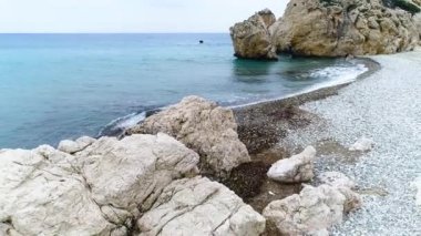 Dalgaların yukarıdaki hava manzarası mavi bir okyanusta sahile çarpıyor. Sakin deniz, güzel sahil manzaralı insansız hava aracı görüntüsü. Okyanusun kayaya çarpması, turizm, tatil ve dinlenme