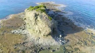Mavi bir denizdeki kayalıkların yukarıdan görünüşü. Okyanus dalgaları güzel kumsalda, hava aracı 4K 'da. Okyanus ıssız dağ kayalarına, turistik yerlere, tatillere ve dinlenmeye çarpıyor.